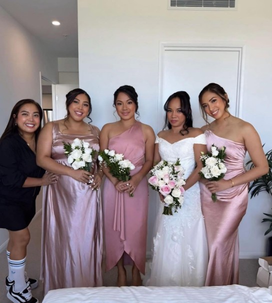 A bride and four bridesmaids in matching pink gowns with their makeup artist